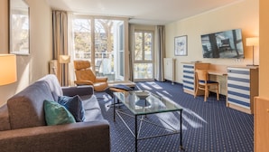 Ett modernt hotellrum med en soffa, en fåtölj och ett litet bord. Det finns ett skrivbord med en stol och en tv som är monterad på väggen.