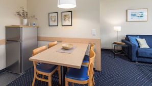 A compact room with a dining table, chairs, a sofa, a lamp, and a refrigerator.