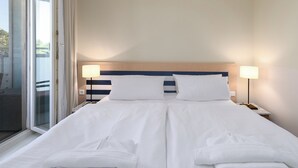 A double bed with white linens, two bedside lamps, and a view of the outdoors through a large window.