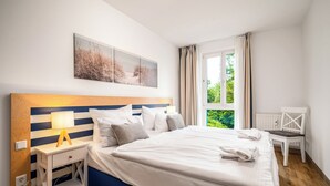 Camera da letto con un letto, comodino, lampada e vista su del verde attraverso una finestra.