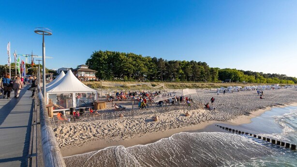 A beach with a tented area, a pier, and a forest in the background. - "Kranichtanz" Vacation Rental with a Balcony and a View Toward the Dike (Zingst)