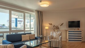 A modern living room with a sofa, armchairs, a glass coffee table, a TV, and a view of the outside. - "Kranichtanz" Vacation Rental with a Balcony and a View Toward the Dike (Zingst)