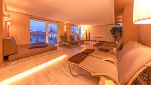 Moderni hotellihuone, josta avautuu panoraamanäkymä kaupunkiin, ja jossa on oleskelualue hierontatuoleineen sekä viihtyisä nurkkaus lampun kanssa.