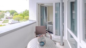Un balcone con tavolo, sedia e vista su una strada e del verde.