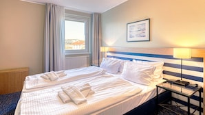 Una camera d'albergo con due letti, una finestra con tende, un comodino con una lampada e un quadro appeso al muro.