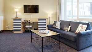 Una camera d'albergo con un divano, un tavolino, una televisione e una scrivania con una sedia.