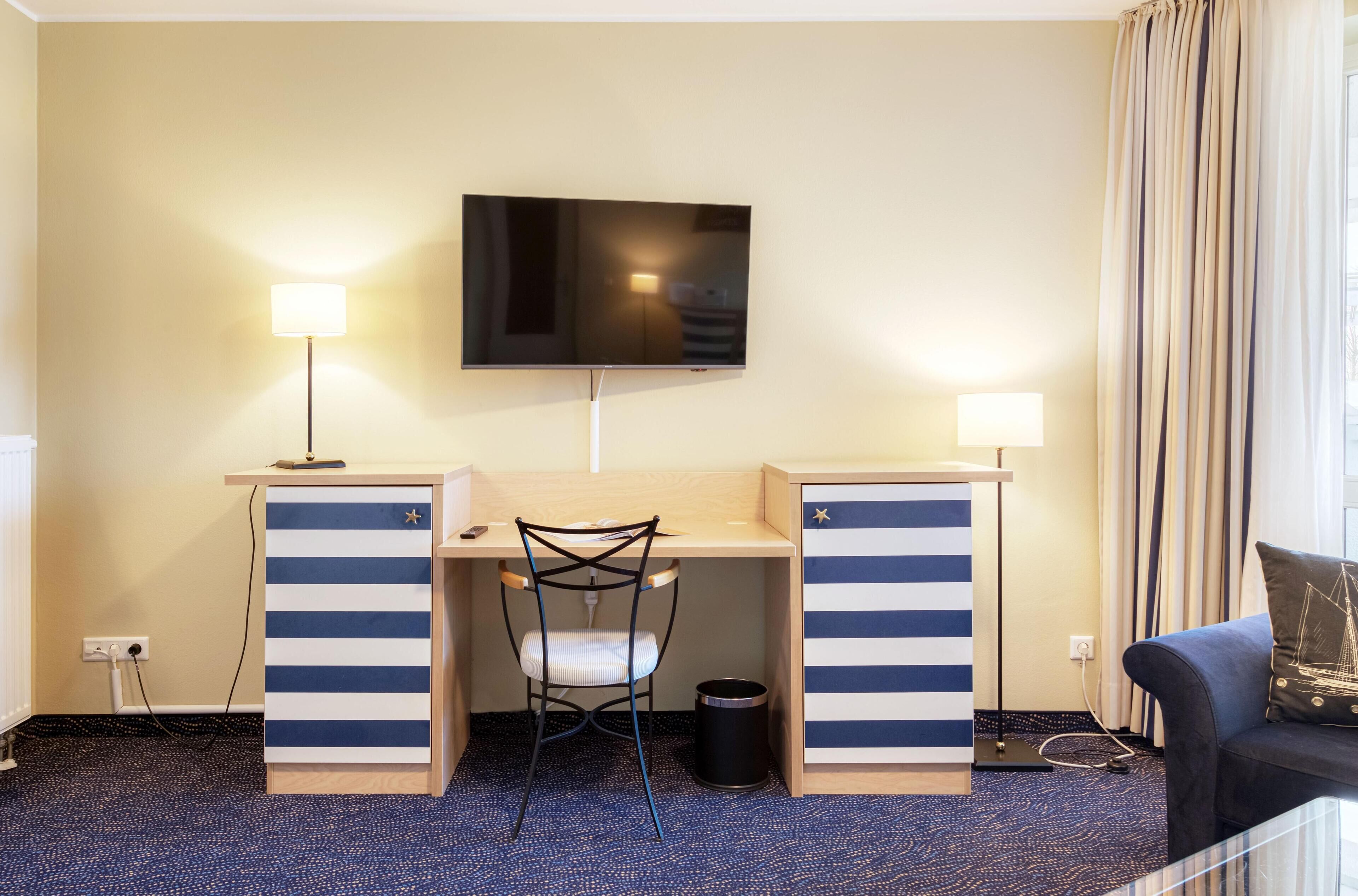 A hotel room with a desk, chair, TV, and a sofa.