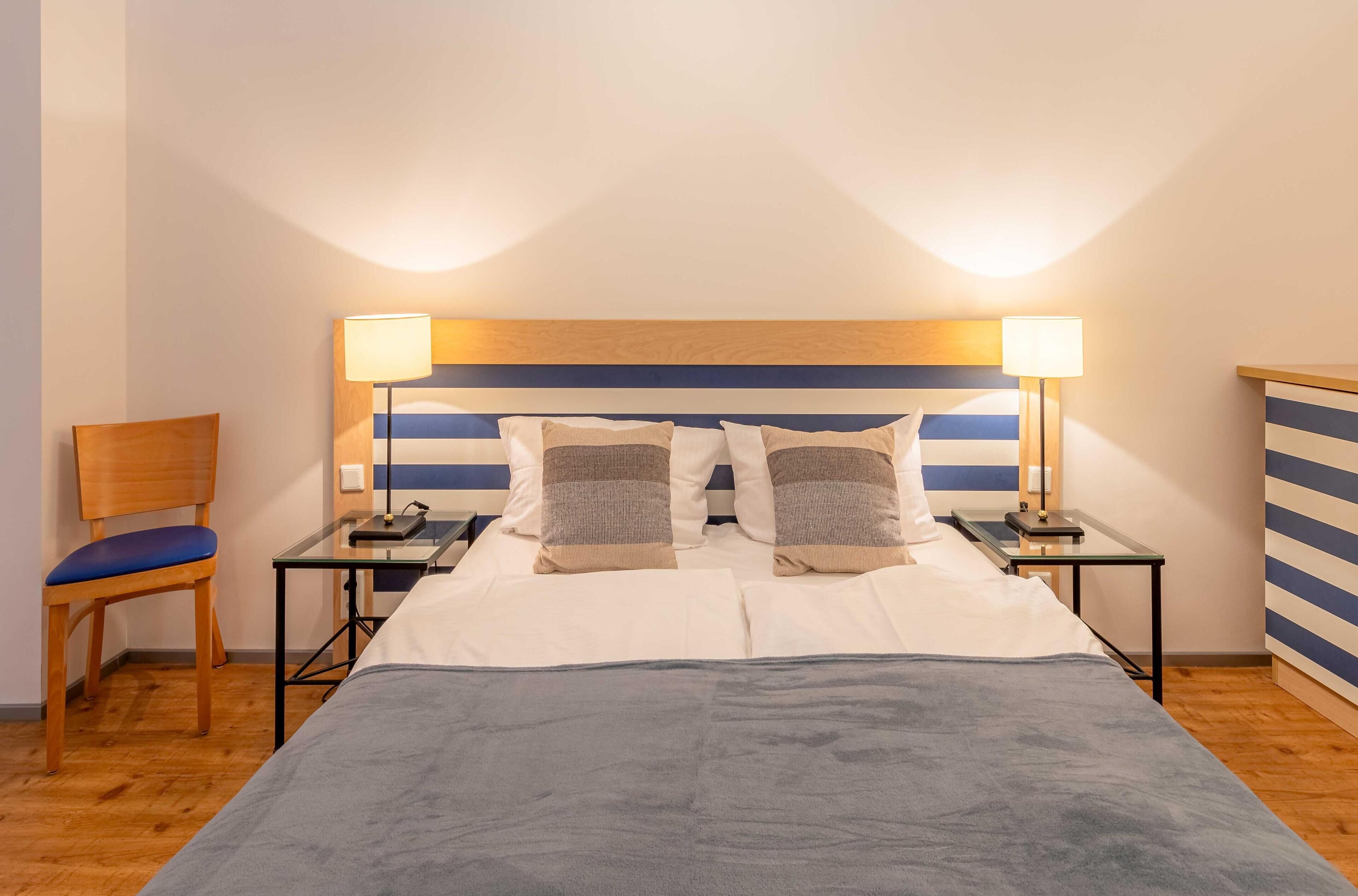 Une chambre d’hôtel avec un lit, deux tables de chevet avec des lampes, une chaise et un mur à rayures.