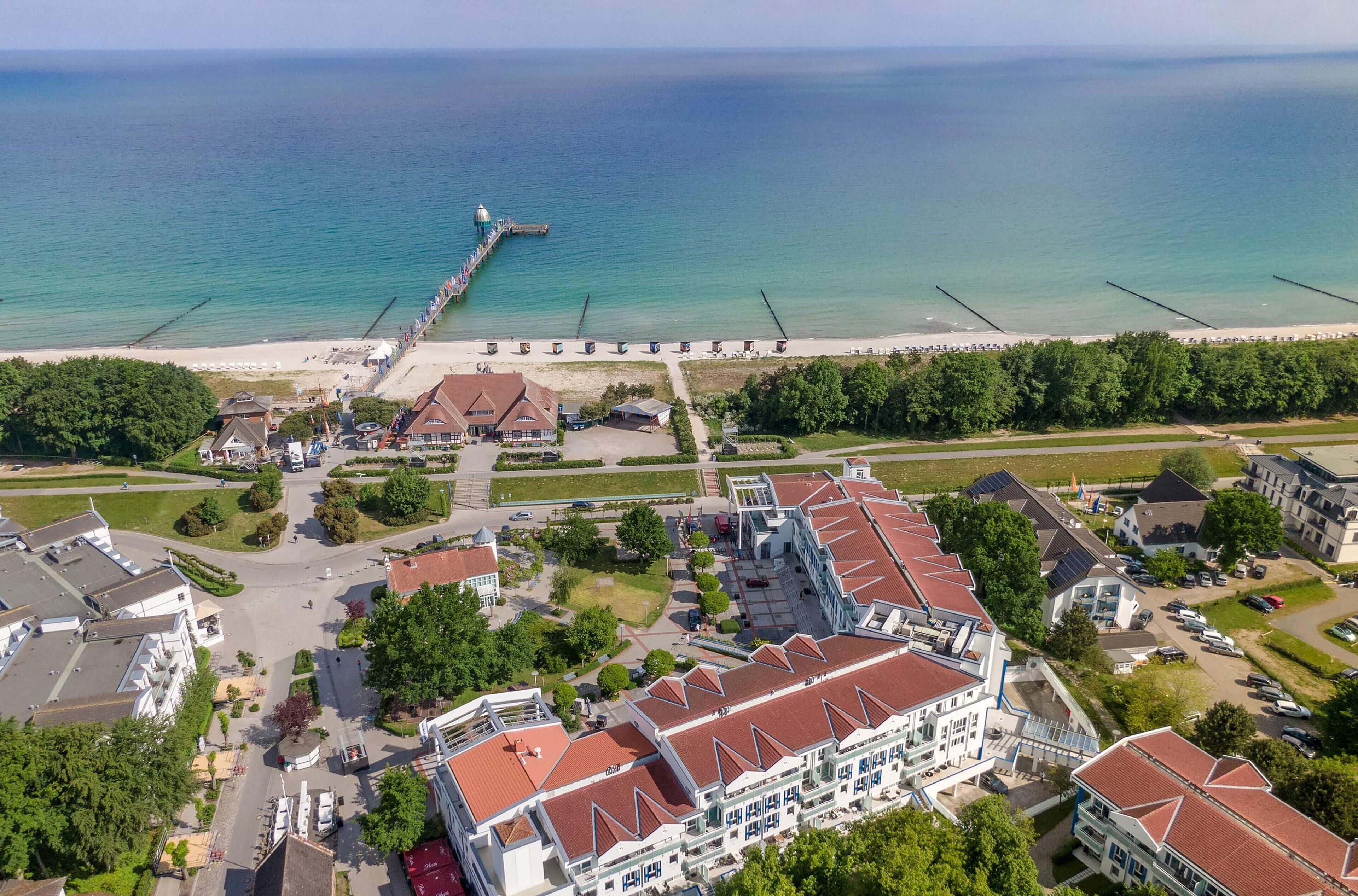 Ein Luftbild einer Küstenstadt mit einem Steg, der sich ins Meer erstreckt, umgeben von Wohngebäuden und einem Strand.
