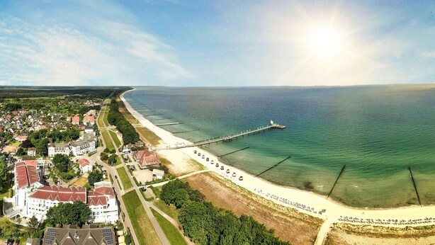 Vista aérea de una zona costera con playa, muelle y un gran complejo de edificios.