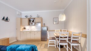 Una cocina compacta con armarios de madera, un refrigerador y un comedor con sillas blancas y una mesa de madera.