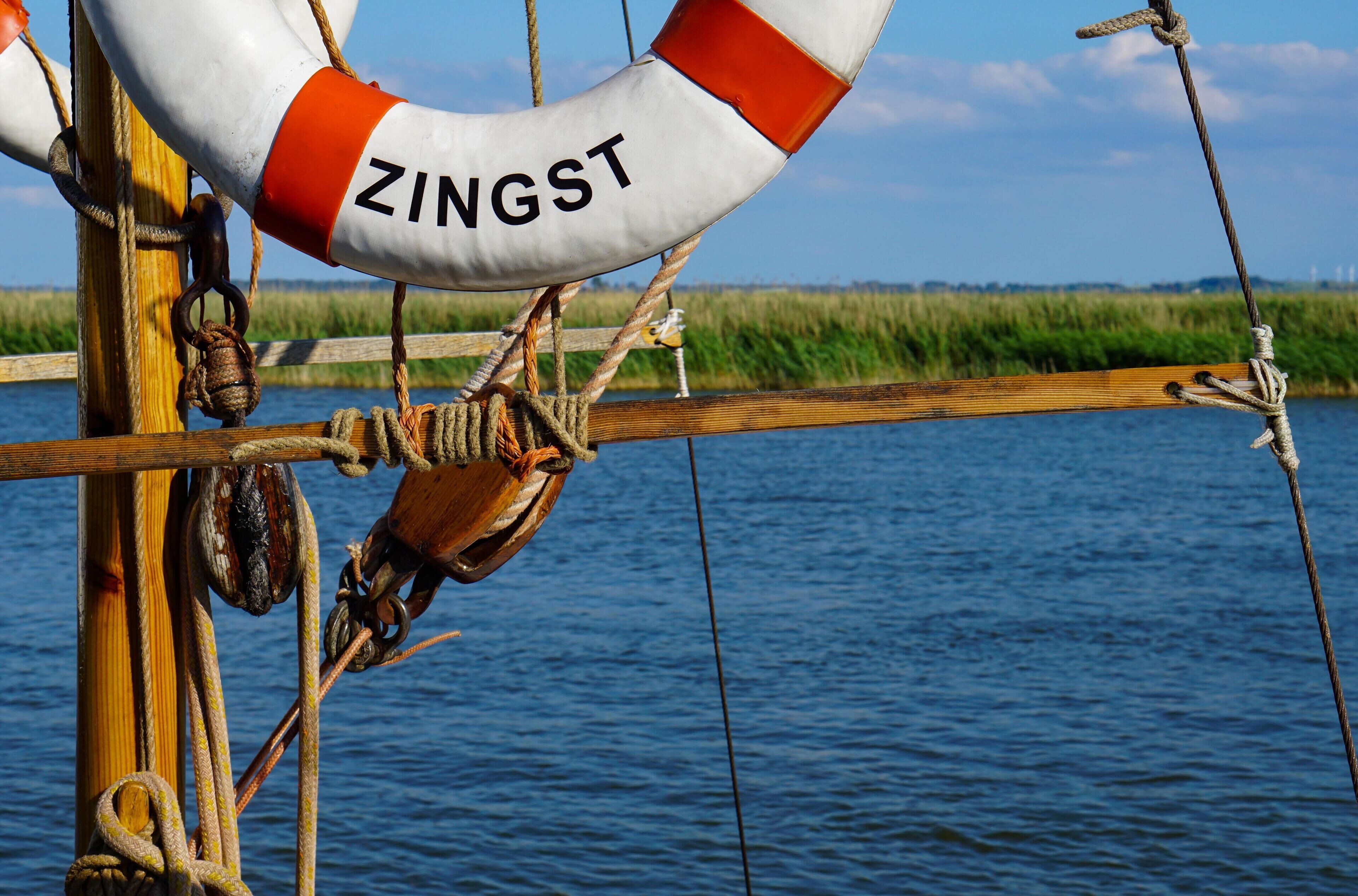 Ein Rettungsring mit dem Schriftzug "ZINGST", an einer Holzkonstruktion in Wassernähe befestigt.