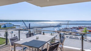 A terrace with a view of the water and boats, outdoor seating, and a building with a sign. - Modern 5-star vacation apartment Müritzsonne with south-west facing balcony and Müritz view (Waren (Müritz))