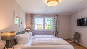 A modern hotel room with a bed, bedside lamps, a chair, a TV, and a window with curtains. - Modern 5-star vacation apartment Müritzsonne with south-west facing balcony and Müritz view (Waren (Müritz))