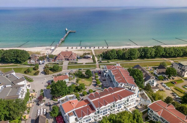 An aerial view of a coastal town with a pier extending into the sea, surrounded by residential buildings and a beach.