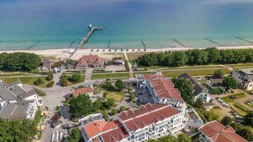 An aerial view of a coastal hotel with multiple buildings, a pier extending into the sea, and a beach in the background.