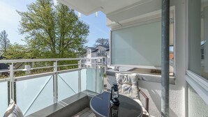 A balcony with a glass railing, a round table with a lantern, and a cushioned seating area.