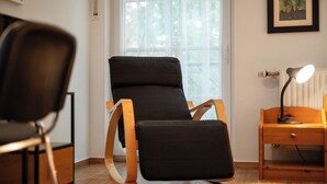 Una habitación moderna con una butaca tapizada de negro, una mesita de madera con una lámpara y una ventana con persianas.