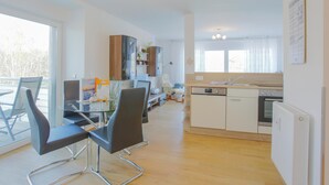 A modern kitchen with a dishwasher, oven, and a dining area with a glass table and black chairs. - Sanddorn vacation apartment - pure relaxation just 200 meters from the Baltic Sea beach (Dierhagen)