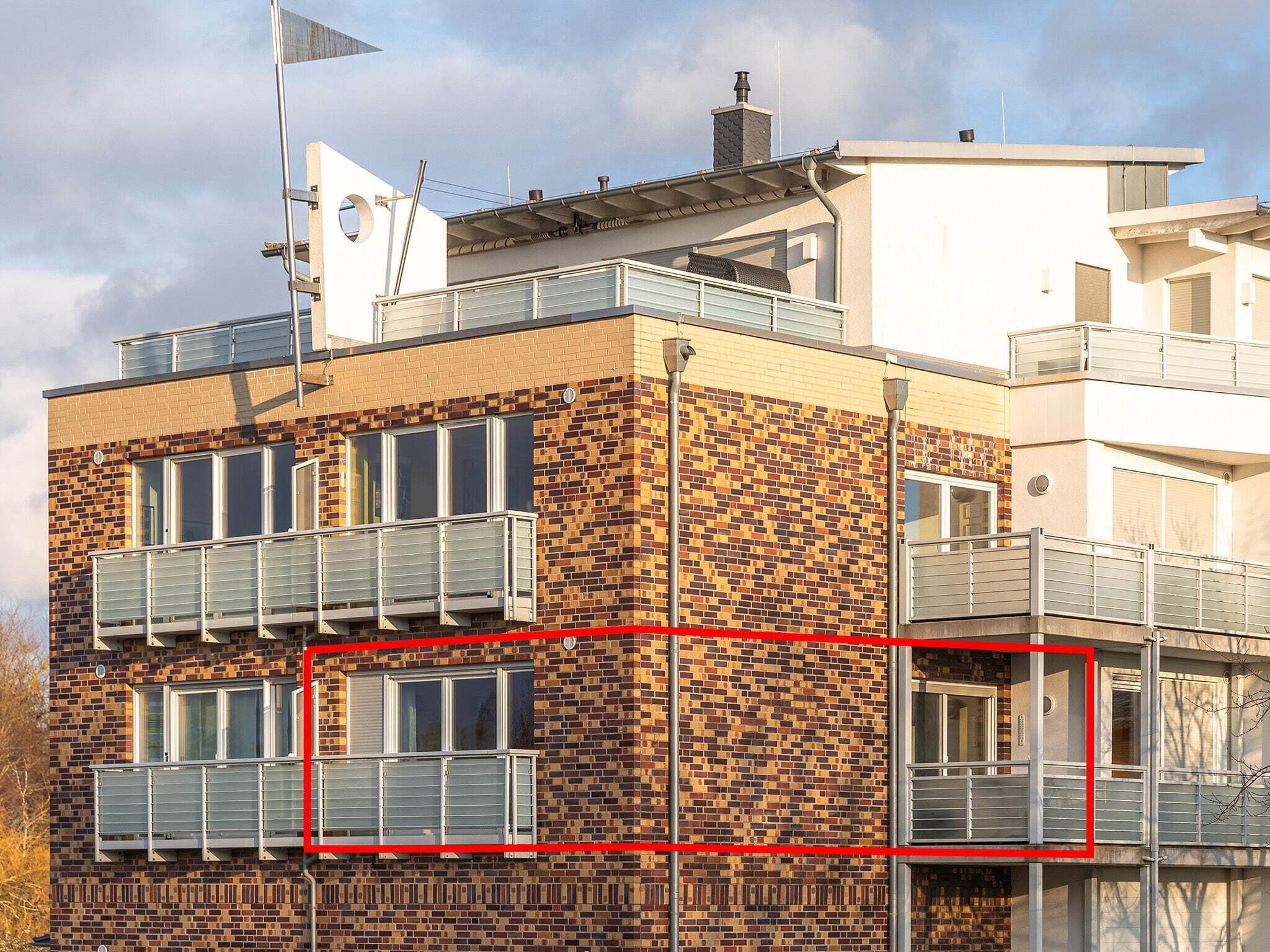 En bygning med flere etager, murstensfacade, altaner med gelændere og et fladt tag med skorsten.