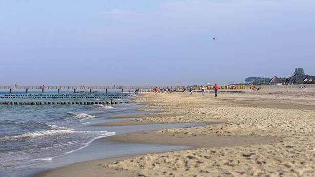 A beach with a pier extending into the water, people walking along the shore, and a clear sky. - Sanddorn vacation apartment - pure relaxation just 200 meters from the Baltic Sea beach (Dierhagen)
