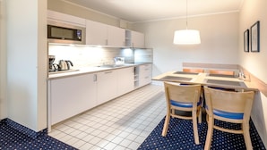 Una cocina compacta con microondas, lavabo y sillas de madera junto a una pequeña mesa de comedor.