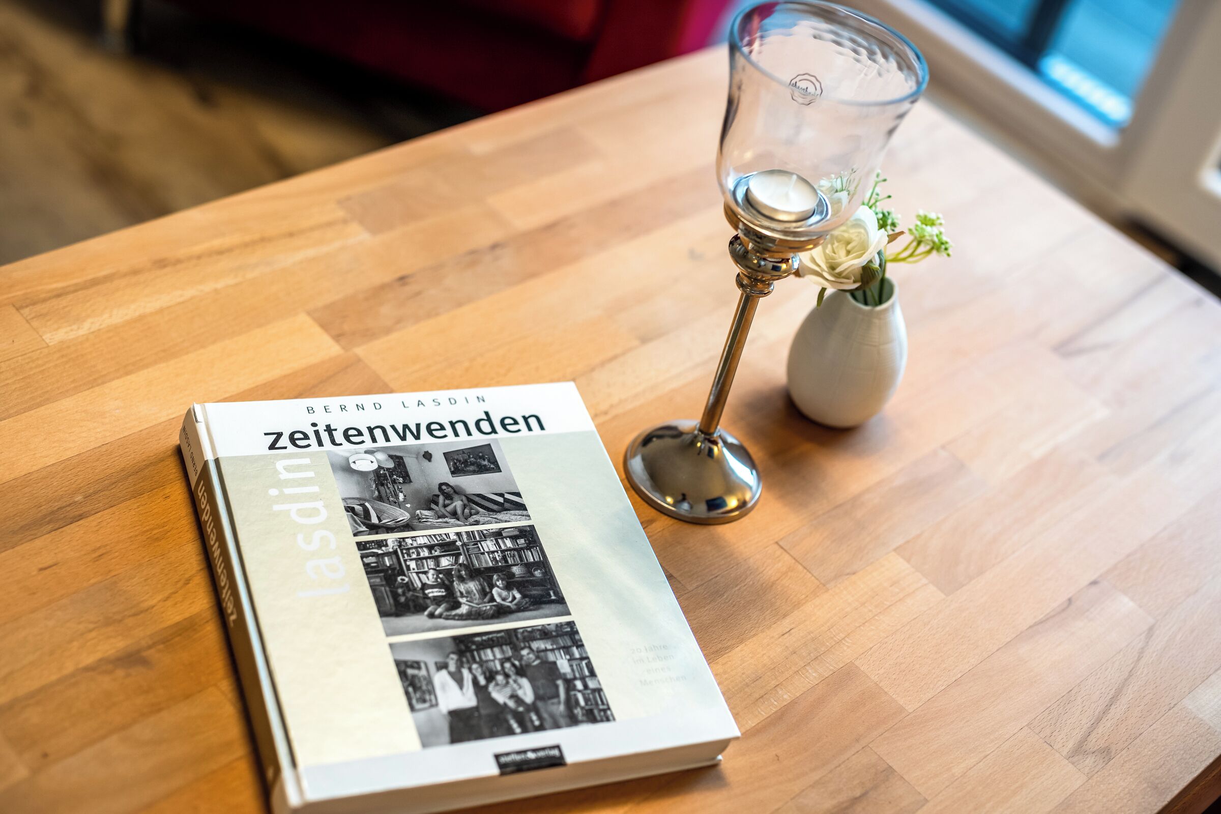 Een boek met de titel 'zeitenwenden' op een houten tafel, naast een glas met bloemdecoratie.