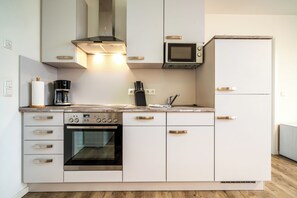 Una cocina moderna con armarios blancos, horno empotrado, microondas y cafetera.