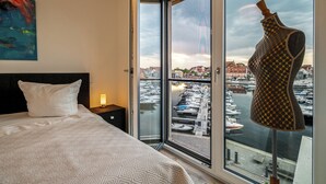A bedroom with a large window, a bed, a nightstand, a lamp, and a mannequin. - Vacation apartment feel-good oasis with panoramic views and right next to the spa (Waren (Müritz))