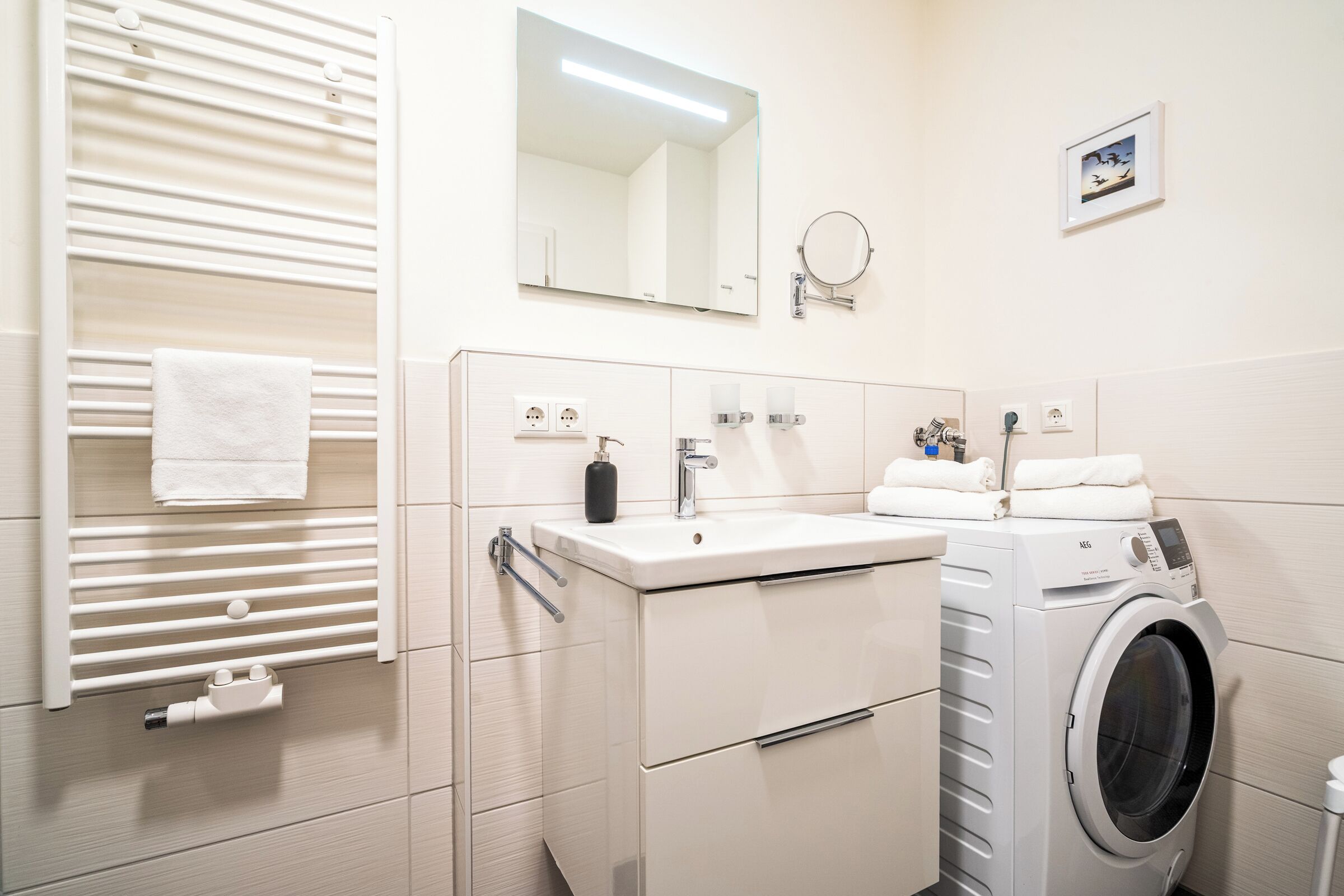 A modern bathroom with a built-in washing machine, a sink, a mirror, and a towel rack.