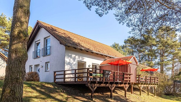Uma casa de dois andares com varanda e deck, rodeada por árvores.