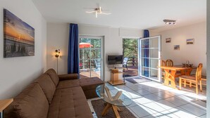 Uma sala de estar moderna com um sofá marrom, uma mesa de centro de vidro, uma televisão e um espaço de jantar com uma mesa e cadeiras de madeira.