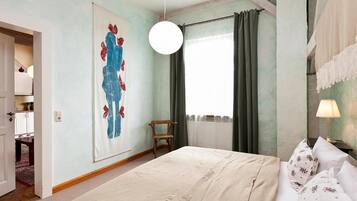 A bedroom with a large bed, a hanging light fixture, a chair, and a painting on the wall.