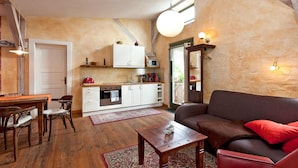 Una sala de estar acogedora con un sofá marrón, una mesa de centro de madera y un comedor con una mesa y sillas de madera. Se ve una cocina con armarios blancos y un microondas al fondo.