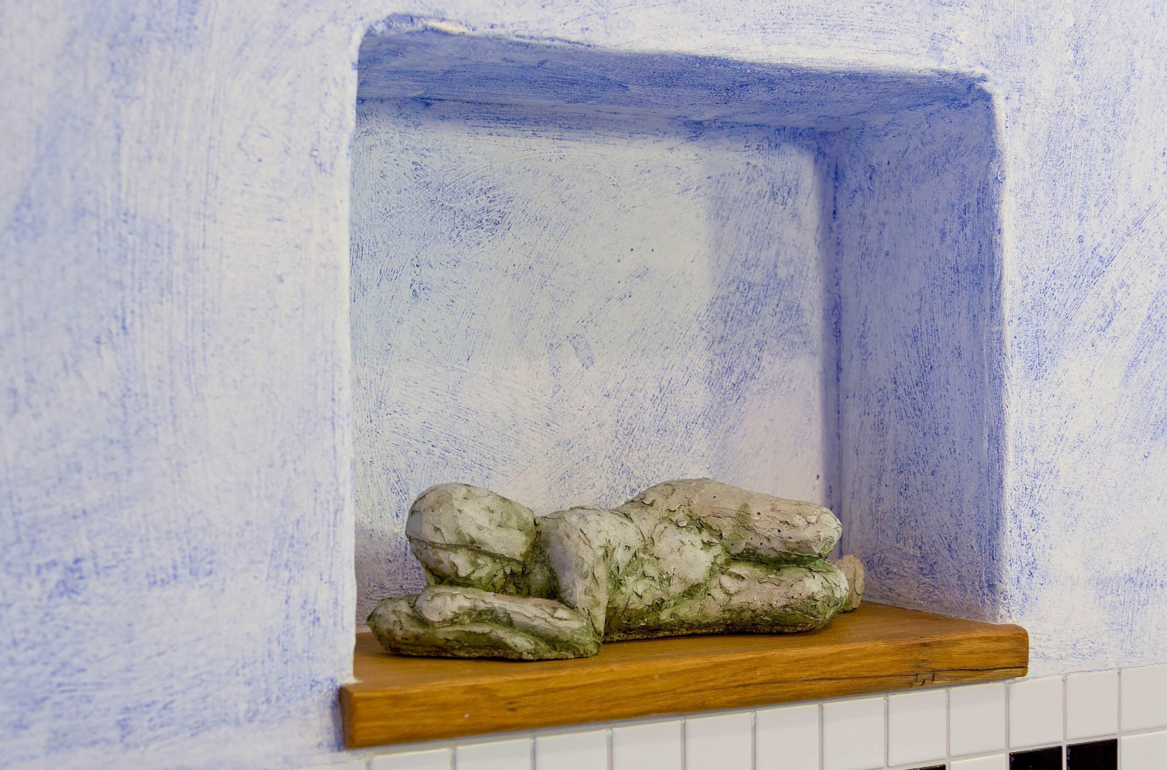 A corner of a room with a white tiled wall and a wooden shelf.