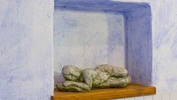 A corner of a room with a white tiled wall and a wooden shelf.