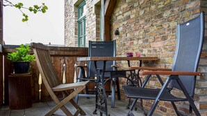 Un patio con una mesa y sillas de madera, una planta en maceta y un muro de ladrillo.