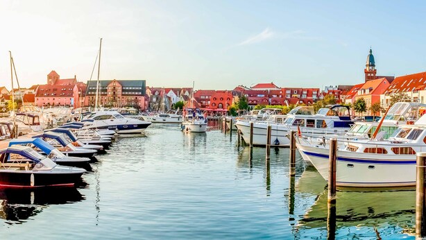 Een jachthaven met boten afgemeerd langs een rustig water, omringd door gebouwen met verschillende architectuurstijlen.