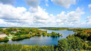 Blick auf einen See mit einem großen Gebäude, Bäumen und blauem Himmel.
