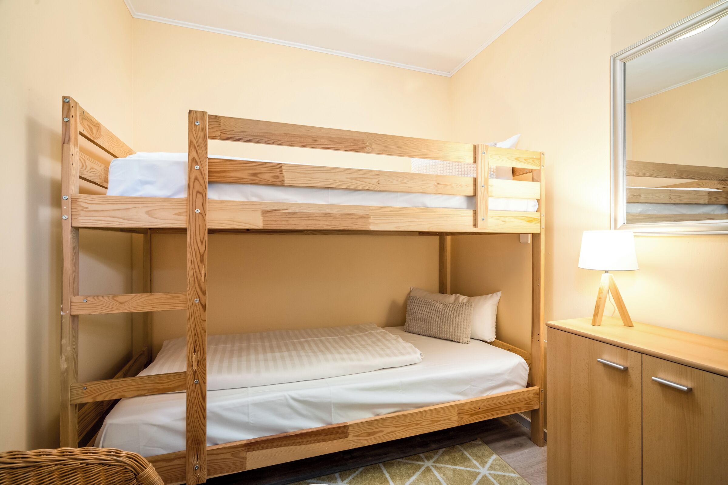 Una cama litera con estructura de madera, una mesita de noche con una lámpara y un espejo en la pared.