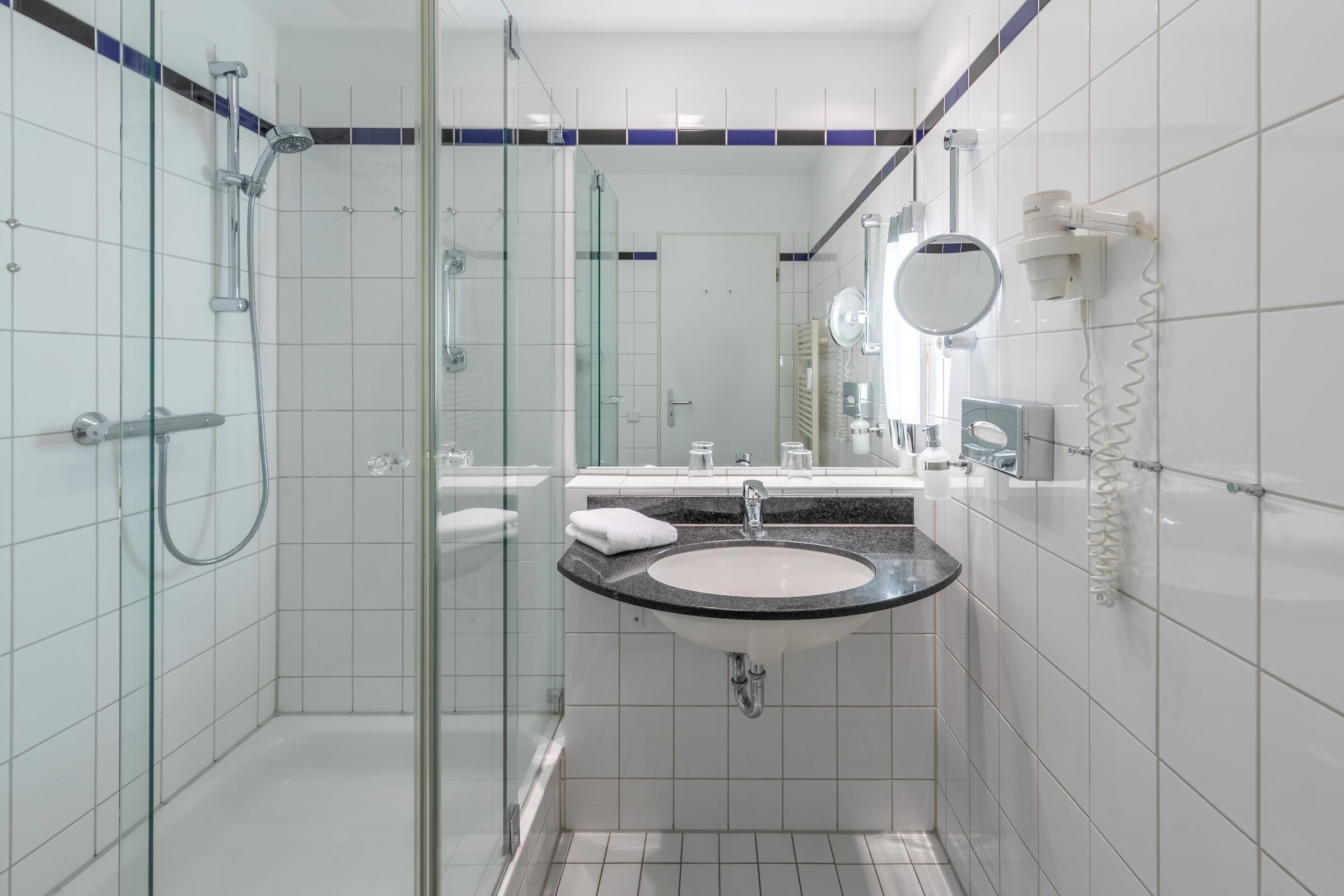 Un baño moderno con ducha envuelta en cristal, lavamanos con encimera de mármol y espejo.