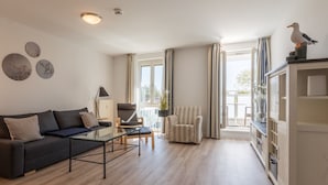 A modern living room with a sofa, coffee table, armchair, and a bookshelf. - "Sturmmöwe" Vacation Apartment at the Zingst Pier (Zingst)
