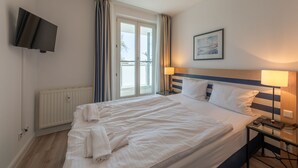 Habitación de hotel con una cama grande, dos mesitas de noche, un televisor de pantalla plana, un radiador y una ventana con cortinas.