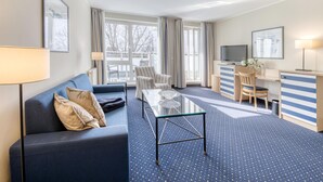 Ein Hotelzimmer mit einer Couch, einem Glastisch, einem Streifenmuster-Schreibtisch, einem Fernseher und Blick ins Freie.