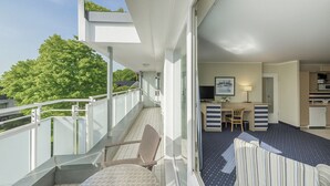 Ein Balkon mit Blick auf Bäume, eine Essecke mit Tisch und Stühlen sowie eine Küchenzeile.