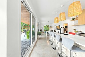 A modern kitchen with a long countertop, bar stools, and pendant lighting.