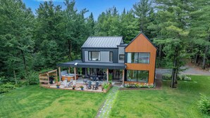 Ein modernes, zweistöckiges Haus mit überdachter Terrasse, Sitzgelegenheiten im Freien und einem Whirlpool.