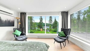 Ein modernes Schlafzimmer mit einem großen Fenster, zwei grauen Sesseln, einem Bett und einer Wand-Klimaanlage.