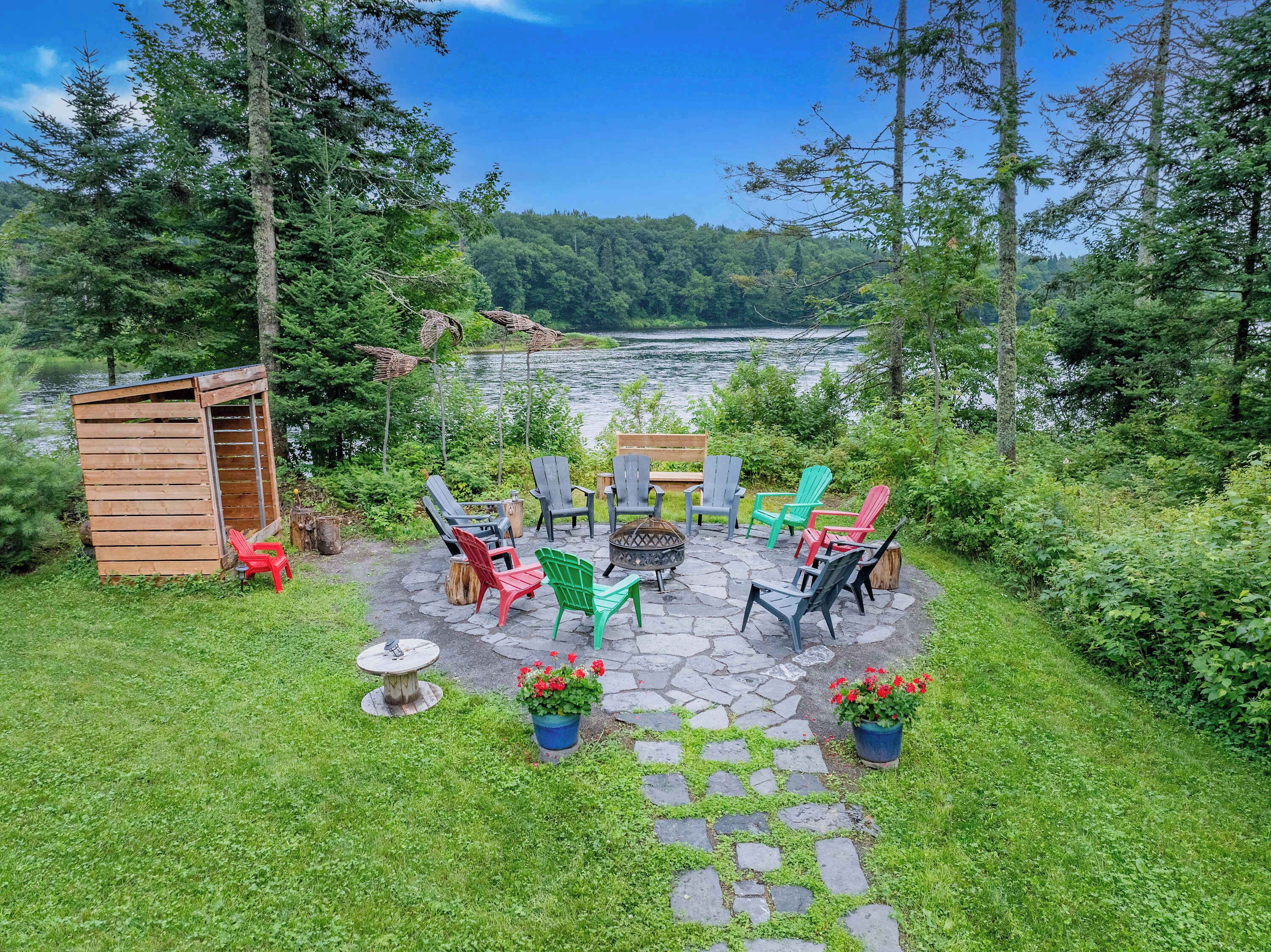 A patio with Adirondack chairs, a fire pit, and a small wooden shed.