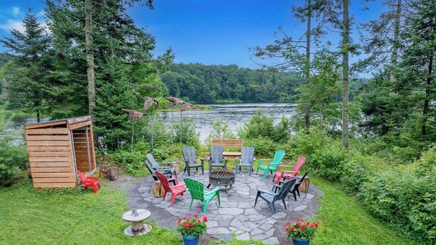 Eine Terrasse mit Adirondack-Stühlen, einer Feuerstelle und einem kleinen Holzschuppen.